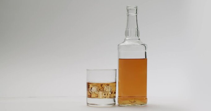 Still life of an elegant glass of whiskey with ice cubes next to a transparent bottle half-full of amber liquid, all isolated on a pristine white background with ample copy space