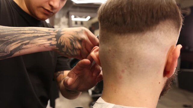 Stylist cutting man's hair with clipper in barbershop, closeup