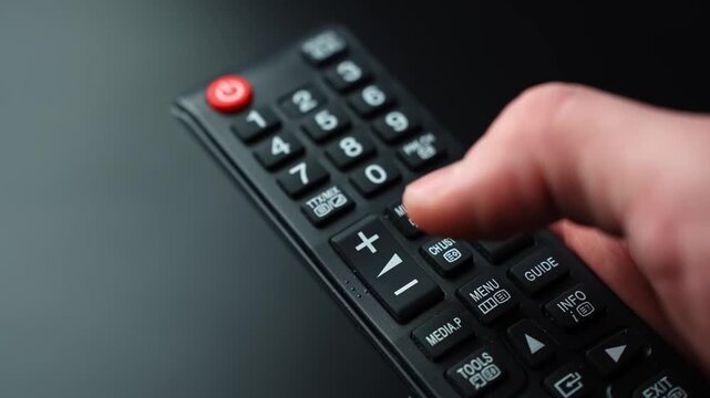 Close-up of a thumb pressing volume down on a TV remote control on a dark background with shallow depth of field and copy space, ideal for streaming, home entertainment, and audio adjustment.