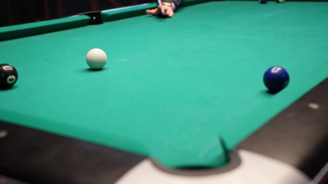 Shallow-focus billiards scene as a player aims the cue ball toward a blue object near the side pocket on green felt, creating a tense, cinematic bar game moment.