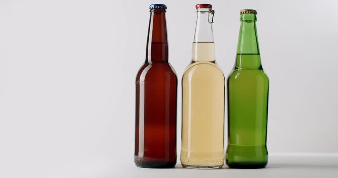 Different beer bottles slowly rotating on white background. Three different colored glass bottles of fresh craft beer with light and dark lager rotating on a turntable isolated on a white background