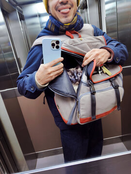 Man taking elevator selfie with cat inside backpack carrier