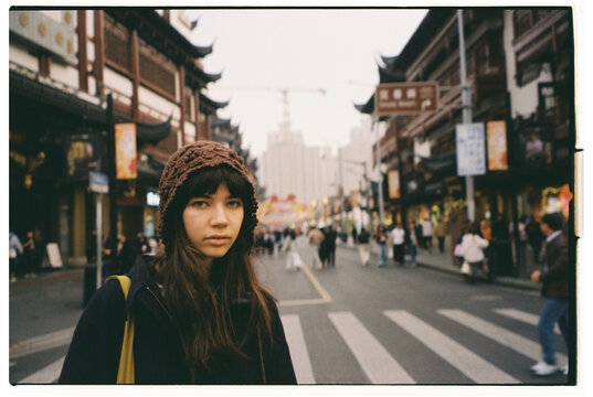 Woman stands in busy street in urban area with shops and buildings