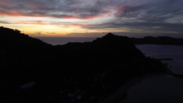 Cinematic drone flight over Guimaras Island in the Philippines at sunrise. The camera moves forward above the tropical island landscape, heading toward glowing sun on the horizon. Warm golden light.