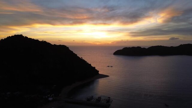 Cinematic drone flight over Guimaras Island in the Philippines at sunrise. The camera moves forward above the tropical island landscape, heading toward glowing sun on the horizon. Warm golden light.