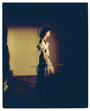 Model walks in costume with bow and arrow in a dimly lit space