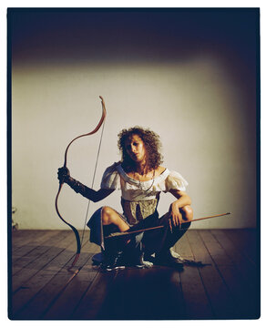 Woman poses with bow and arrow in indoor setting 