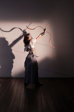 Person practices archery indoors with a bow and arrow in a dim room
