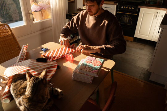 Man wrapping gifts at table