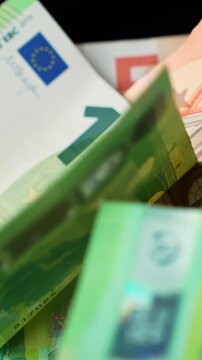 Vertical close-up of euro banknotes on a black table as a hand slides and stacks notes, rich concept for payment, wealth, and personal finance.