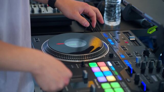 Close-up of professional DJ hand scratching vinyl record on black Pioneer CDJ controller with colorful performance lights and mixer in nightclub live set