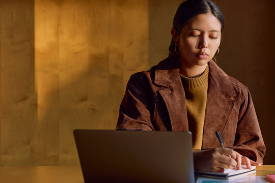 Woman working on laptop at desk in warm office light