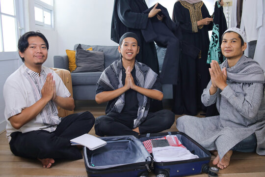 Three Happy Asian Muslim Men Sitting On Floor With Greeting Gesture During Preparing For Mudik