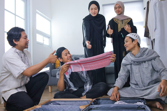 Smiling Young Muslim People Showing Thumbs Up Gesture While Packing Suitcase For Mudik