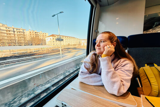 Woman Looks out the Window While Riding a Train in a City