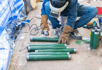 A metalworker uses a handheld power angle grinder to cut through a green steel pipe.