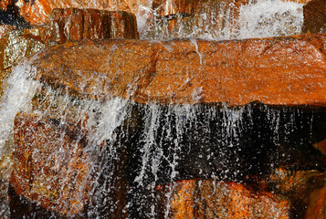 Obraz premium Waterfall background close-up. Drops of water flowing down rocks from waterfall. Water flows over rocks creating small splashes as it moves down a stream. This scene shows the beauty of wild nature.