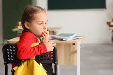 Selbstklebende Fototapeten Altes Krankenhaus Beelitz Little schoolgirl biting nails at desk in classroom  © Pixel-Shot