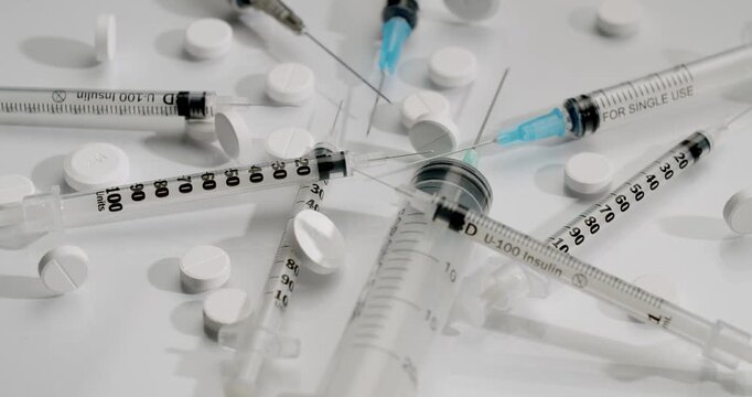 Medical insulin syringes with needles and white pills rotating on a white background, healthcare treatment, and pharmaceutical industry. Insulin syringes and pills isolated on a white background.