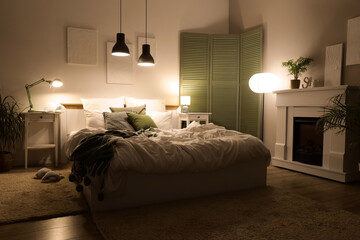 Fototapeta premium Interior of bedroom with folding screen, fireplace and glowing lamps at night