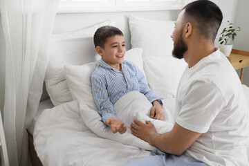 Obraz premium Happy father with his son in pajamas speaking on bed at home