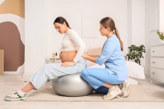 Young doula with pregnant woman training on fitball in bedroom