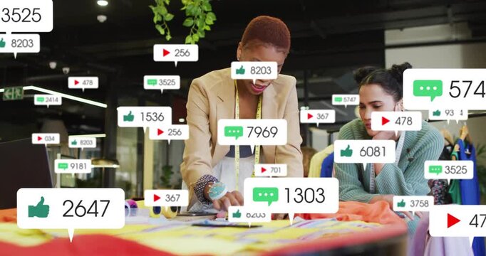Designers working at table measuring fabric, laptop pinging social icons over subjects for fashion