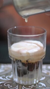 Vertical screen Asian Barista Drizzling Salted Cream Topper. Slow Glossy Droplet Falls From Pitcher Onto Whipped Foam, Hand Visible Guiding Pour, Closeup Texture Of Foam And Salted Sheen,