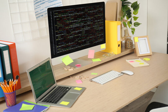 Computer monitor and laptop with codes on programmer's desk in light office