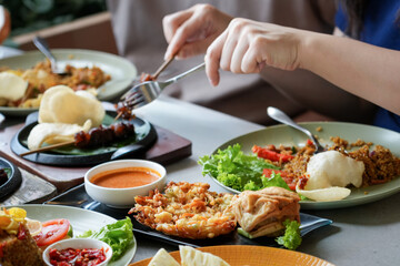 Close up of person sharing a traditional Indonesian meal with Ayam Bakar grilled chicken, sate skewers, and bakwan fritters.