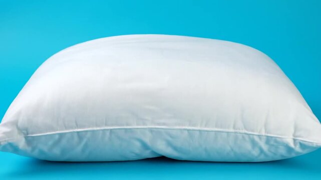 Hand pressing down on a soft white pillow, demonstrating its plushness and comfort on a blue background.