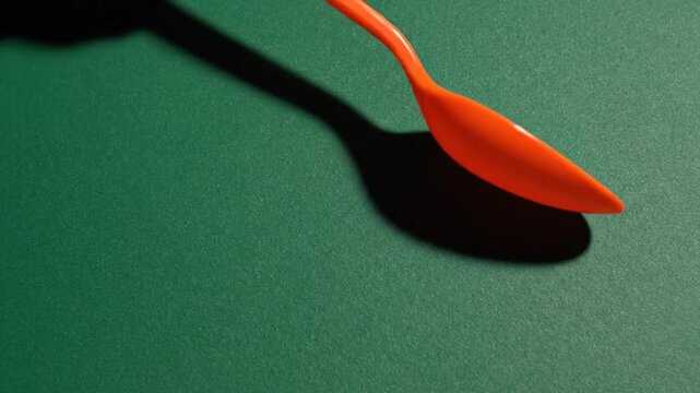 Orange Plastic Spoon on Green Background with Shadow.