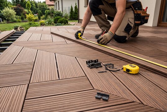 Construction worker measuring and installing brown WPC decking boards with a geometric pattern