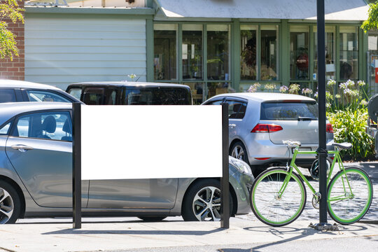 Blank outdoor advertising mockup sign board or billboard on a suburban street with parked cars and a bicycle in an urban building. Background texture of public signage or information notice.Copy space