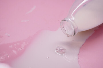 Bottle pours milk on pink surface with drip pattern