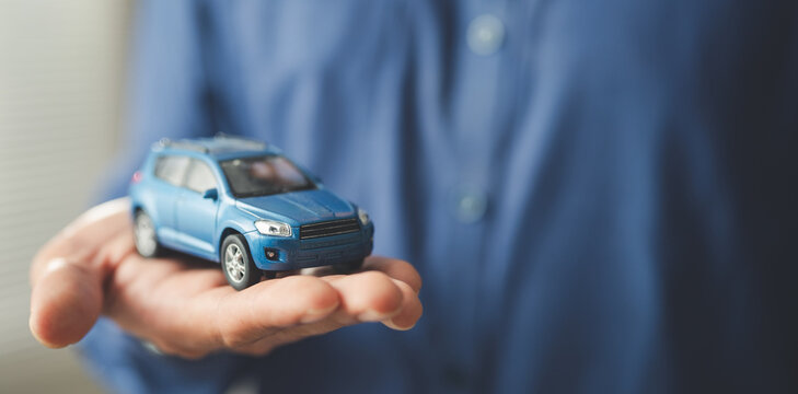 Hand holding a miniature car symbolizing car purchase, auto loan, and vehicle insurance. Concept of dealership agreement, financial planning, ownership, and secure transportation investment.