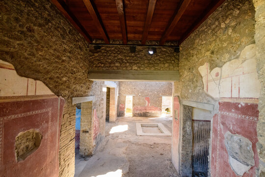 Sunlight filters into the ancient atrium of the House of Julia Felix in Pompeii, Italy, highlighting faded Roman frescoes, textured stone walls, and a central impluvium. The rustic interior features