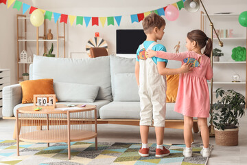 Little brother and sister sticking paper fish to each other's backs at home. April Fool's Day prank