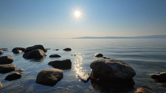 82.Tranquil landscape featuring glassy lake water stretching toward the horizon, shoreline rocks in the foreground, warm sun overhead, and faint silhouettes of faraway land.