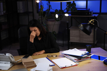 Tired Asian businesswoman sitting at table and working in office