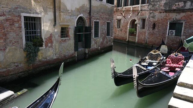 Gondolas Navigating Narrow Venetian Canals. A picturesque scene of traditional black gondolas gliding through a narrow, quiet canal in Venice