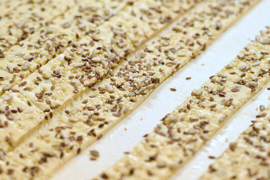 Cracker dough ribbons on conveyor belt showcasing strips with sesame seeds and sunflower seeds in a bakery production area