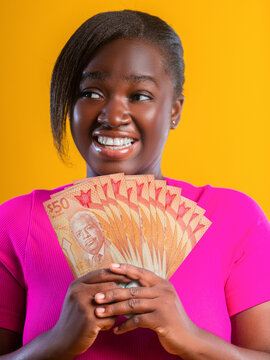 A woman smiles as she fans out orange Barbados 50-dollar banknotes. The notes feature Errol Barrow, the "Father of Independence," set against a bright yellow background for a cheerful, wealthy feel.