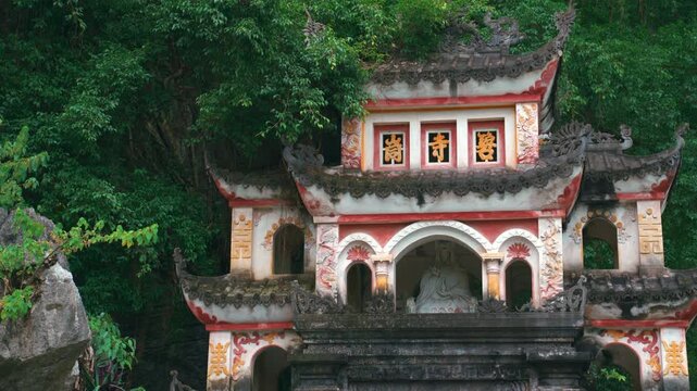 Close-up of the decorated facade of the Bich Dong pagoda, showing traditional reliefs and Buddhist statues integrated into the mountain in Ninh Binh, Vietnam.