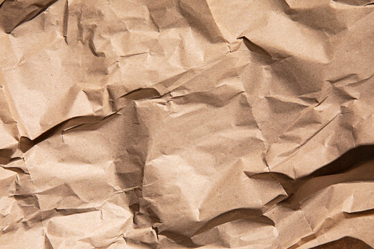 Close-up texture of crumpled brown kraft paper with dramatic shadows and highlights