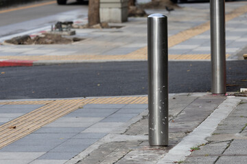 A pole is on the sidewalk next to a crosswalk. The pole is silver and has a yellow stripe....