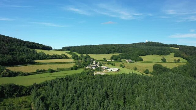 Scenic aerial view of rural farmland, forests, and small village in the Morvan region under a clear blue sky. Lush green fields and dense woodland create a tranquil summer atmosphere.