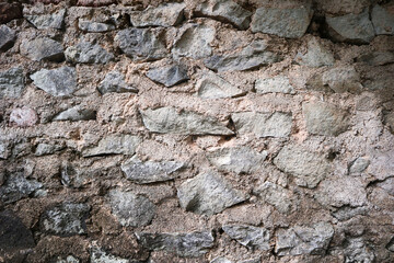 Fototapeta premium Close-up of a rugged retaining wall built from irregular grey stones embedded in a coarse, sandy beige mortar, showing natural geological textures.