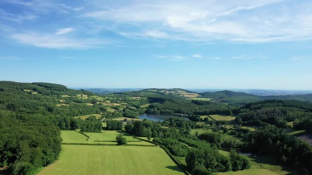 Aerial view of lush green fields, forests, and a tranquil lake in the rural Morvan region under a blue sky. Idyllic summer landscape with gentle hills and natural beauty.