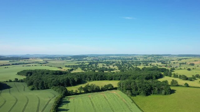 Wide aerial landscape of the Nivernais countryside with green fields, patches of forest, and clear blue sky. Rural farmland and natural scenery under bright daylight.